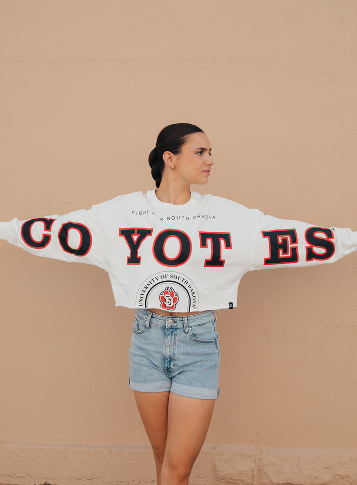 White long sleeve with black and red text, 'COYOTES' across arms and chest and text on torso that says, 'FIGHT FOR SOUTH DAKOTA' and 'UNIVERSITY OF SOUTH DAKOTA' in black