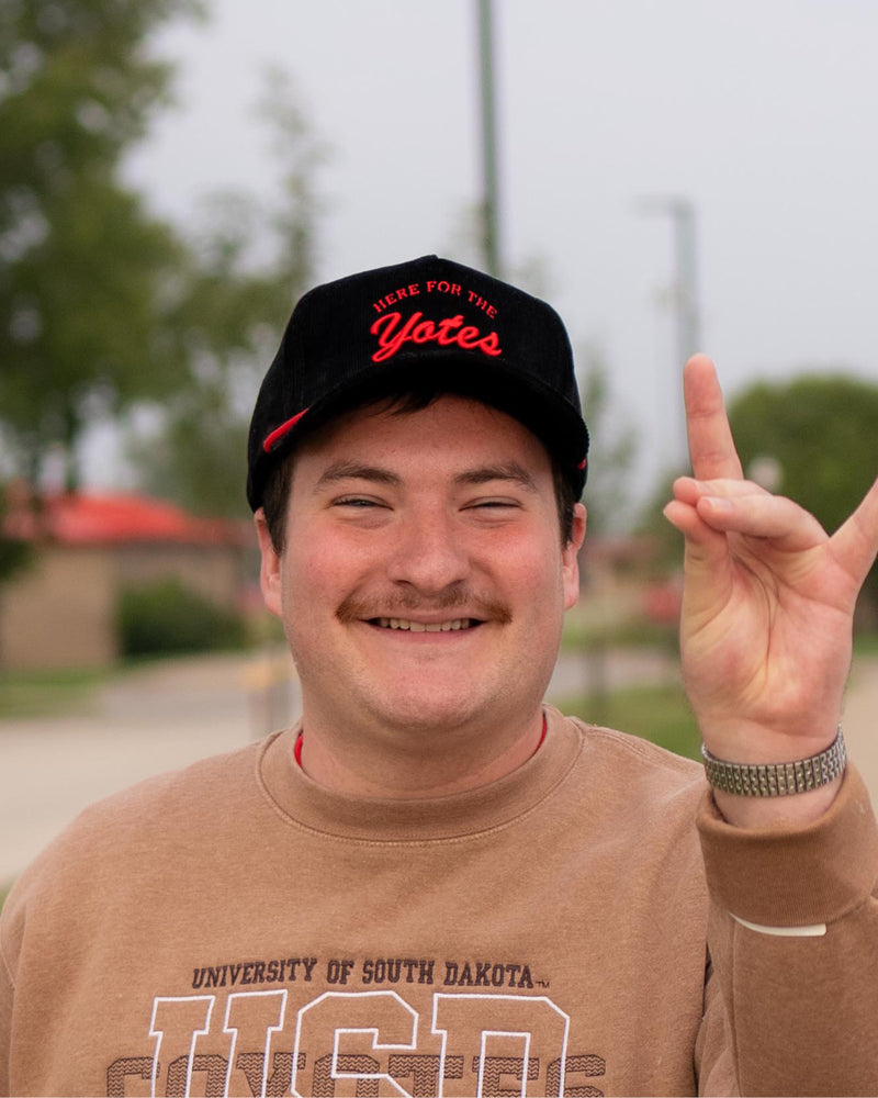 Person wearing the black corduroy cap, with red rope and red embroidered 'HERE FOR THE Yotes.'