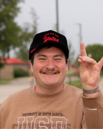 Person wearing the black corduroy cap, with red rope and red embroidered 'HERE FOR THE Yotes.'