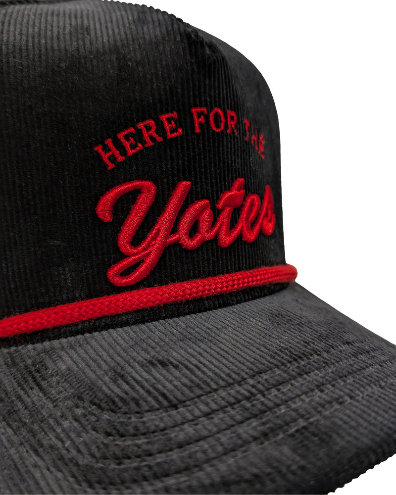 Close-up view of black corduroy cap, with red rope and red embroidered 'HERE FOR THE Yotes.'