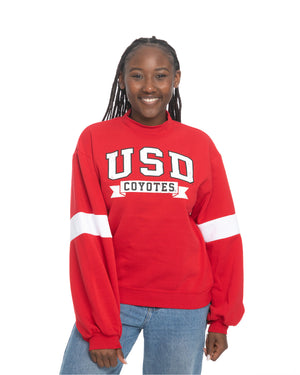 Young woman wearing the red mock neck crew with wide white stripes on sleeves and large design across chest, 'USD COYOTES.'