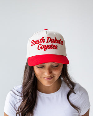 Person wearing a cream hat red embroidered script 'South Dakota Coyotes' and a red bill. 