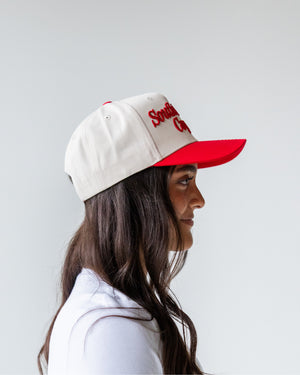 Side view of person wearing a cream hat red embroidered script 'South Dakota Coyotes' and a red bill. 