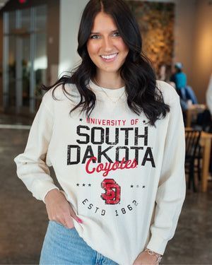 Woman wearing the waffle ivory crew with red and black design, 'UNIVERSITY OF SOOUTH DAKOTA Coyotes ESTD 1862,' with SD logo and stars.