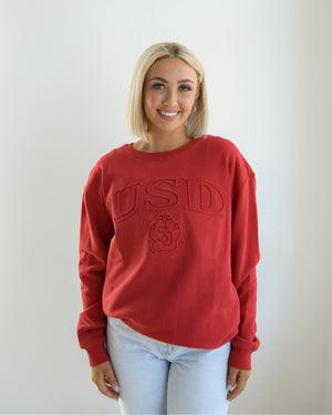 Woman wearing red crew with embossed outlined letters, 'USD,' and SD Paw logo.