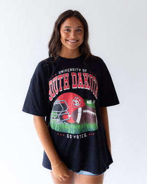 Person wearing a black oversized 'University of South Dakota' t-shirt with football graphics.