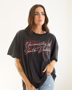 Woman wearing the black oversized tee with red block letter, 'COYOTES,' and white script over it, 'University of South Dakota.'