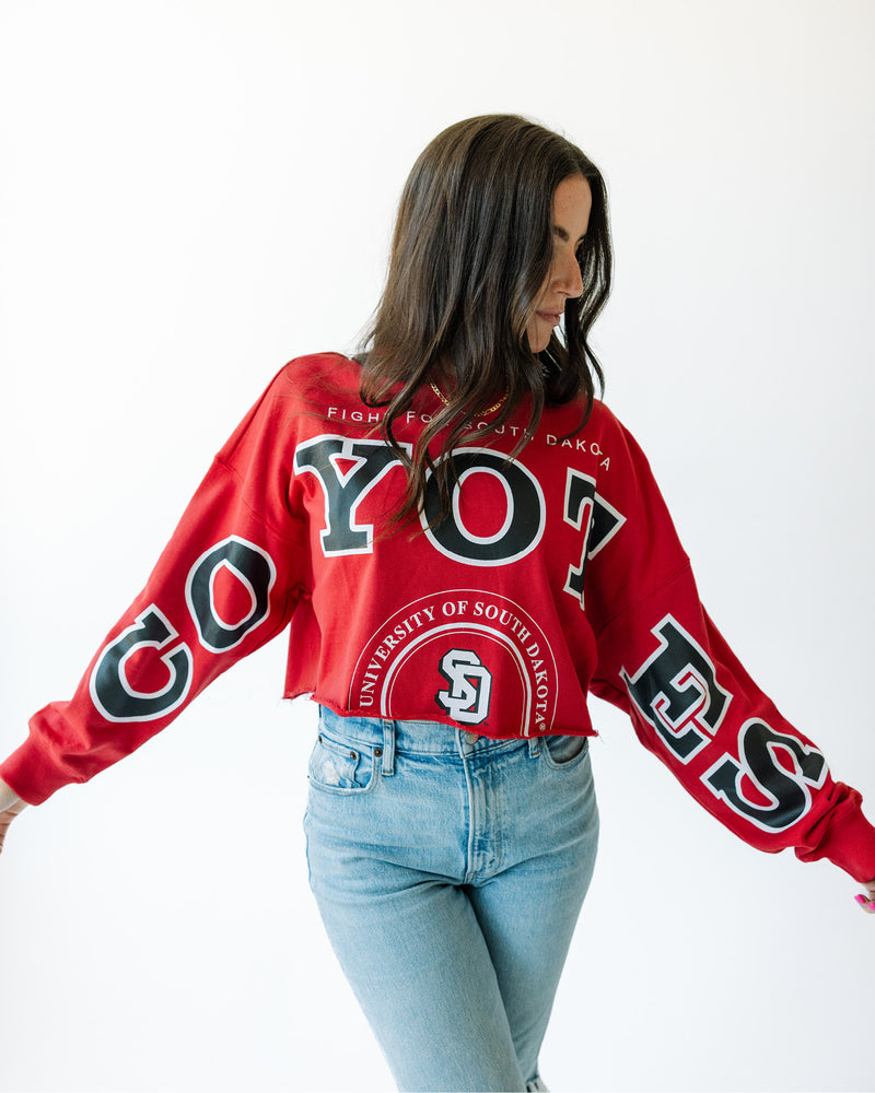 Red long sleeve with black and white text, 'COYOTES' across arms and chest and text on torso that says, 'FIGHT FOR SOUTH DAKOTA' and 'UNIVERSITY OF SOUTH DAKOTA' in white.