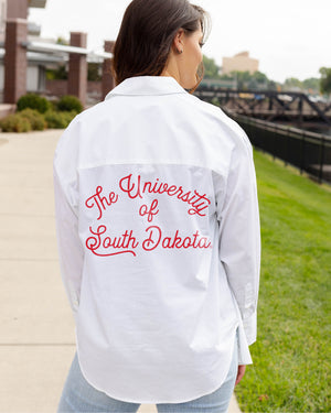 Back of woman wearing white button up with script text on back in red, 'The University of South Dakota.'