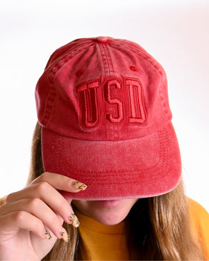 Woman wearing red canvas tonal hat with red, 'USD,' embroidered on front. 