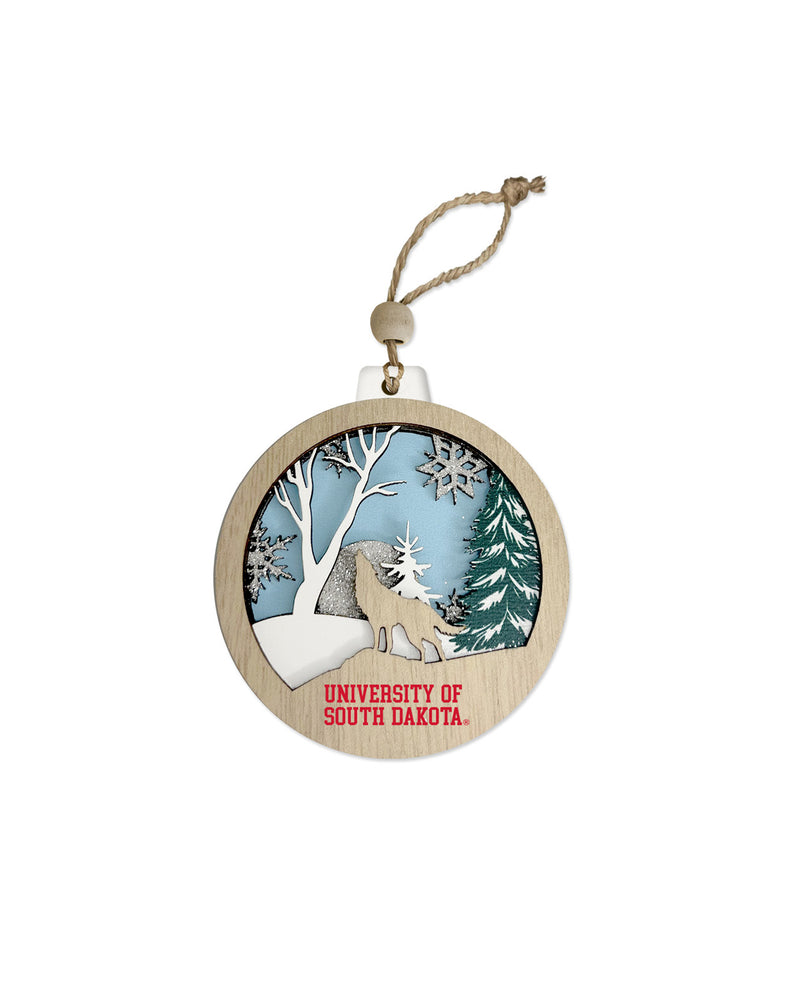 Wooden ornament with a winter scene including the silhouette of a coyote howling and 'University of South Dakota' text near bottom.
